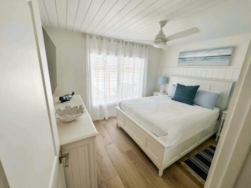 Home Remodeling Contractor in Etters, PA Bright coastal-style bedroom remodel with white paneled ceiling, wood-look floors, white furniture, and large window with sheer curtains