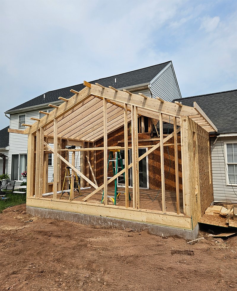 Framing stage of home addition construction with exposed wood beams and pitched roof — EA Building & Remodeling in York PA.