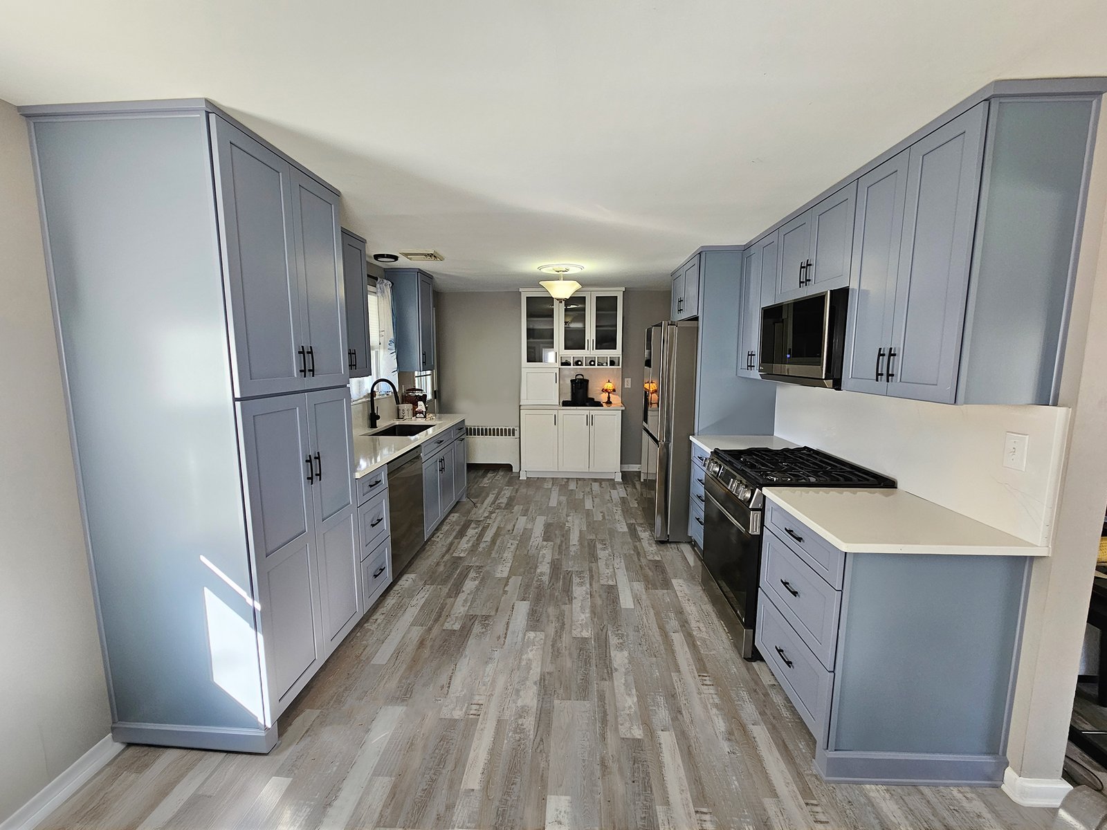 Modern kitchen remodel in York PA with blue shaker cabinets, quartz countertops, stainless steel appliances, and gray wood-look flooring