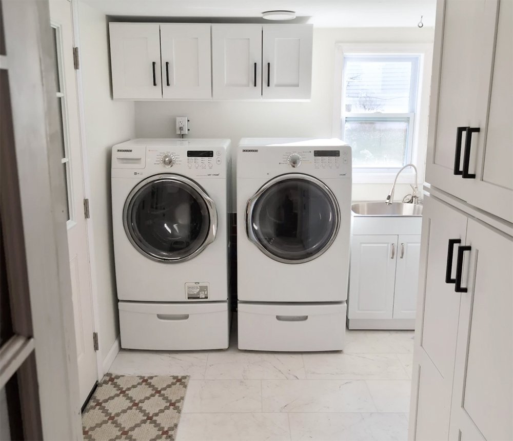 Completed garage-to-laundry-room conversion in York, PA, featuring white cabinetry, insulated flooring, front-loading washer and dryer, utility sink, and added storage.